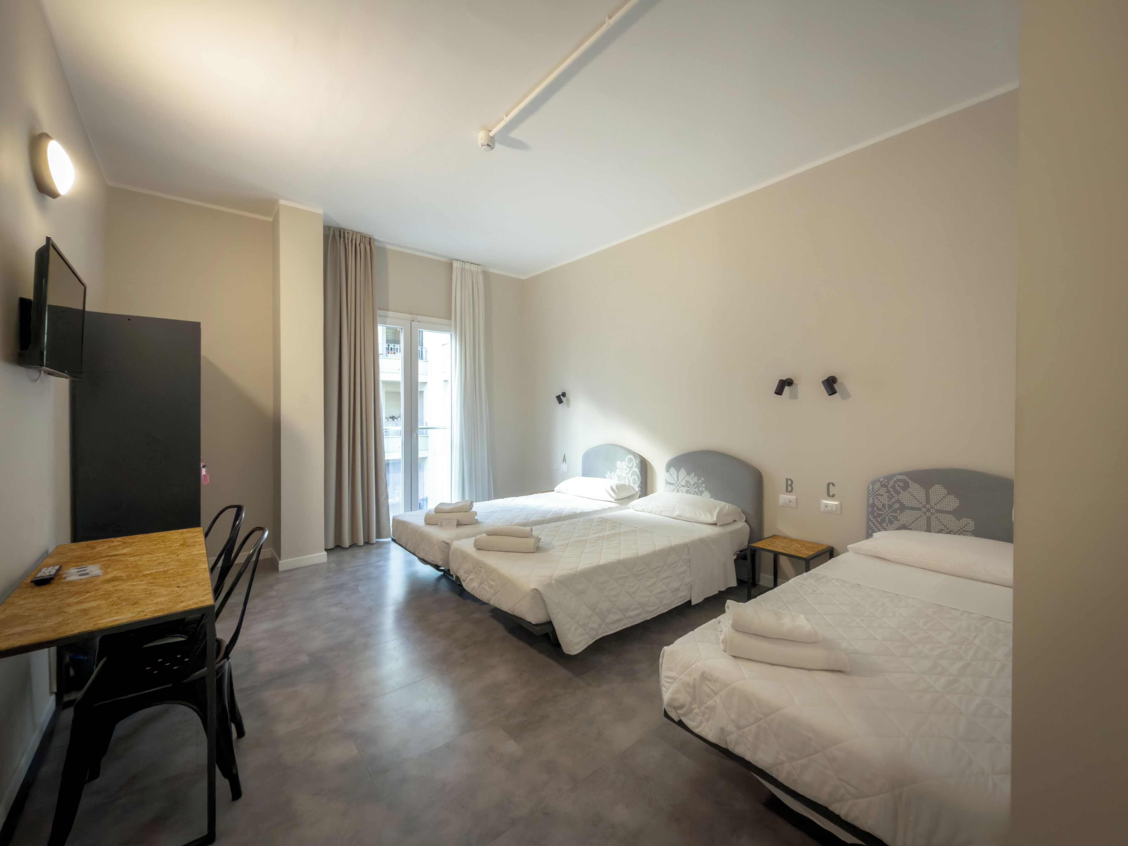 A hotel room with two beds, a desk, a chair, and a TV mounted on the wall.