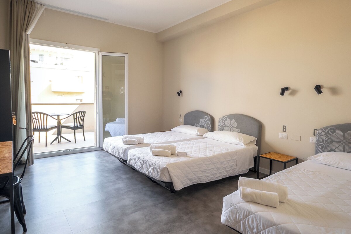 A hotel room with two beds, a small table, chairs, and a balcony.
