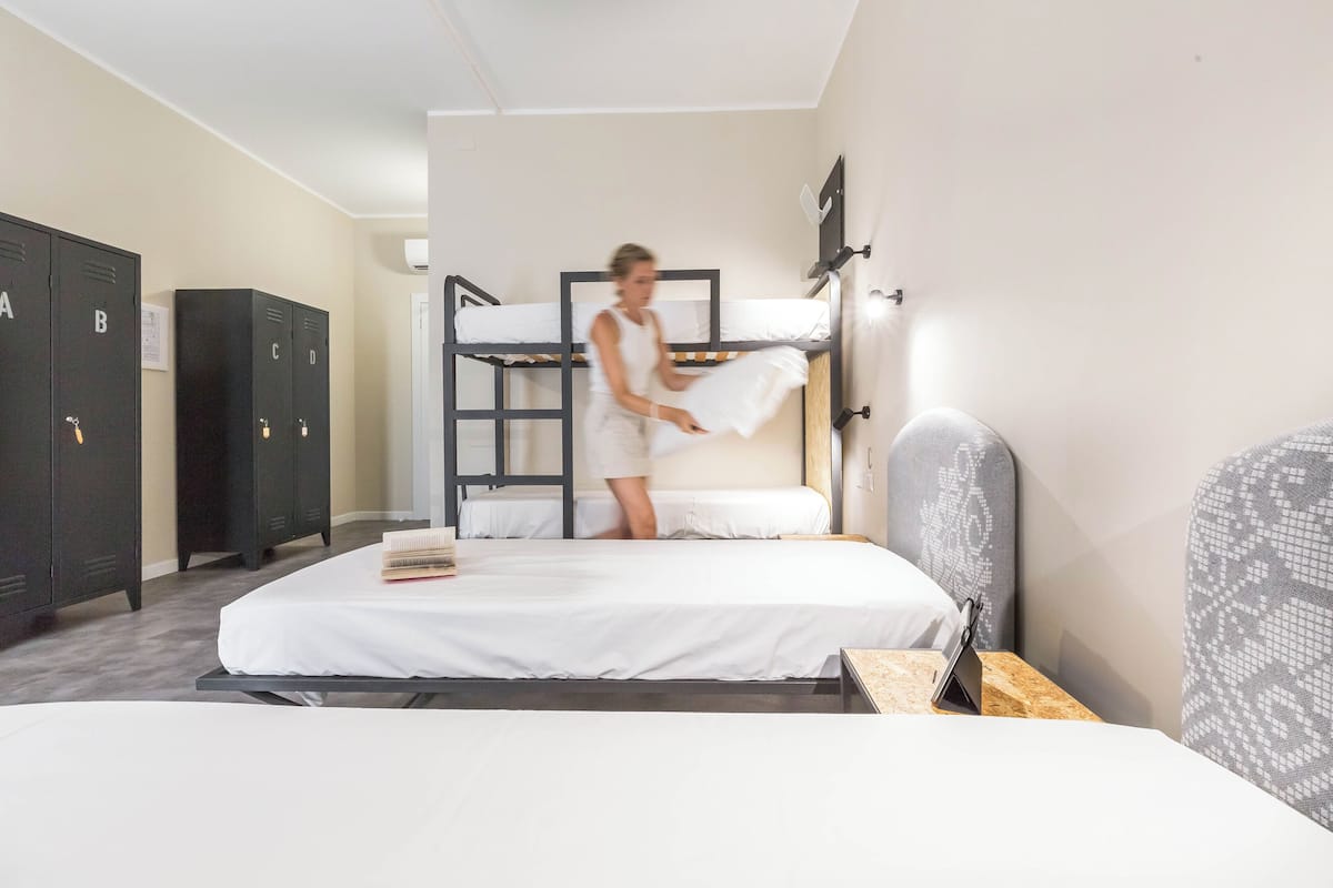 A hotel room with bunk beds, a wooden nightstand, a mirror, and a wardrobe with lettered doors.