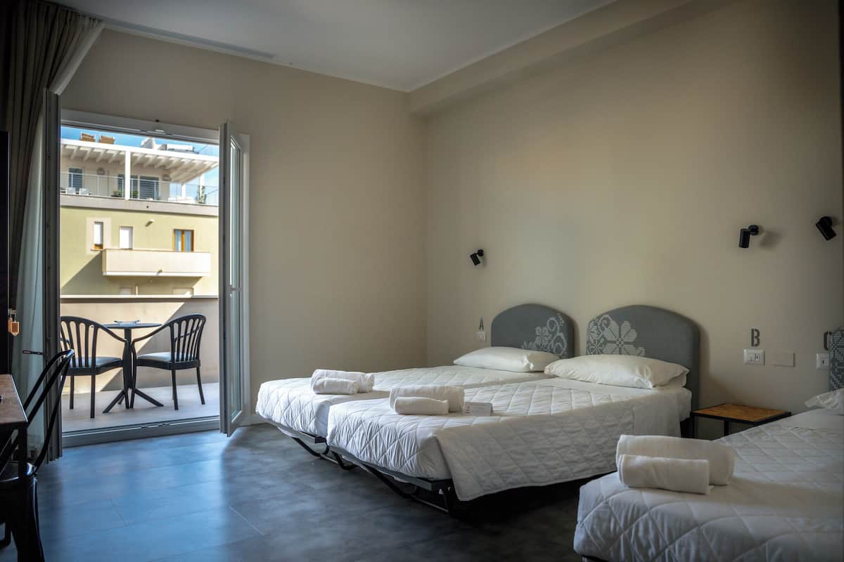 A hotel room with two beds, a balcony with chairs, and a view of a building.