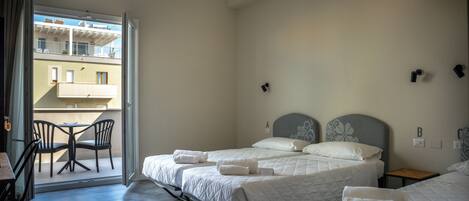 A hotel room with two beds, a balcony with chairs, and a view of a building.