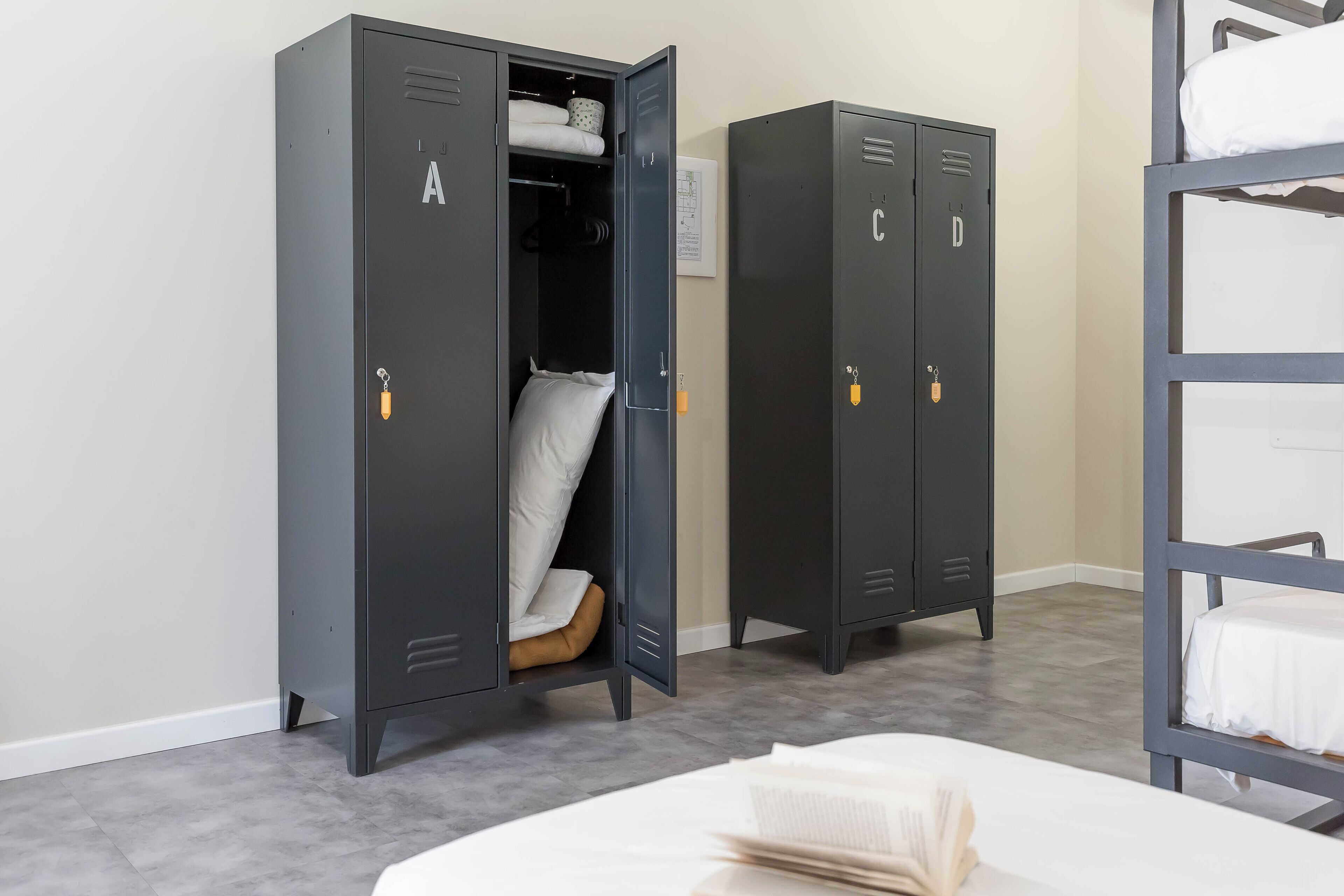 A room with two grey lockers, a bunk bed, and a white bed.