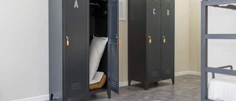 A room with two grey lockers, a bunk bed, and a white bed.