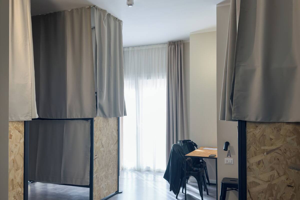 A modern, minimalist room with a wooden floor, a desk with a chair, and a large window with curtains.