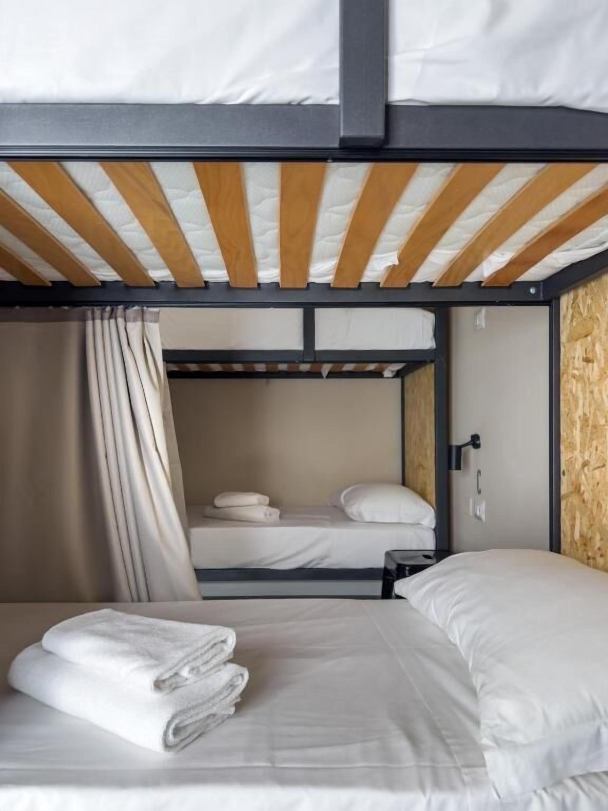 Habitación con literas de madera, un techo de madera, una cortina y toallas dobladas con cuidado en la litera inferior.