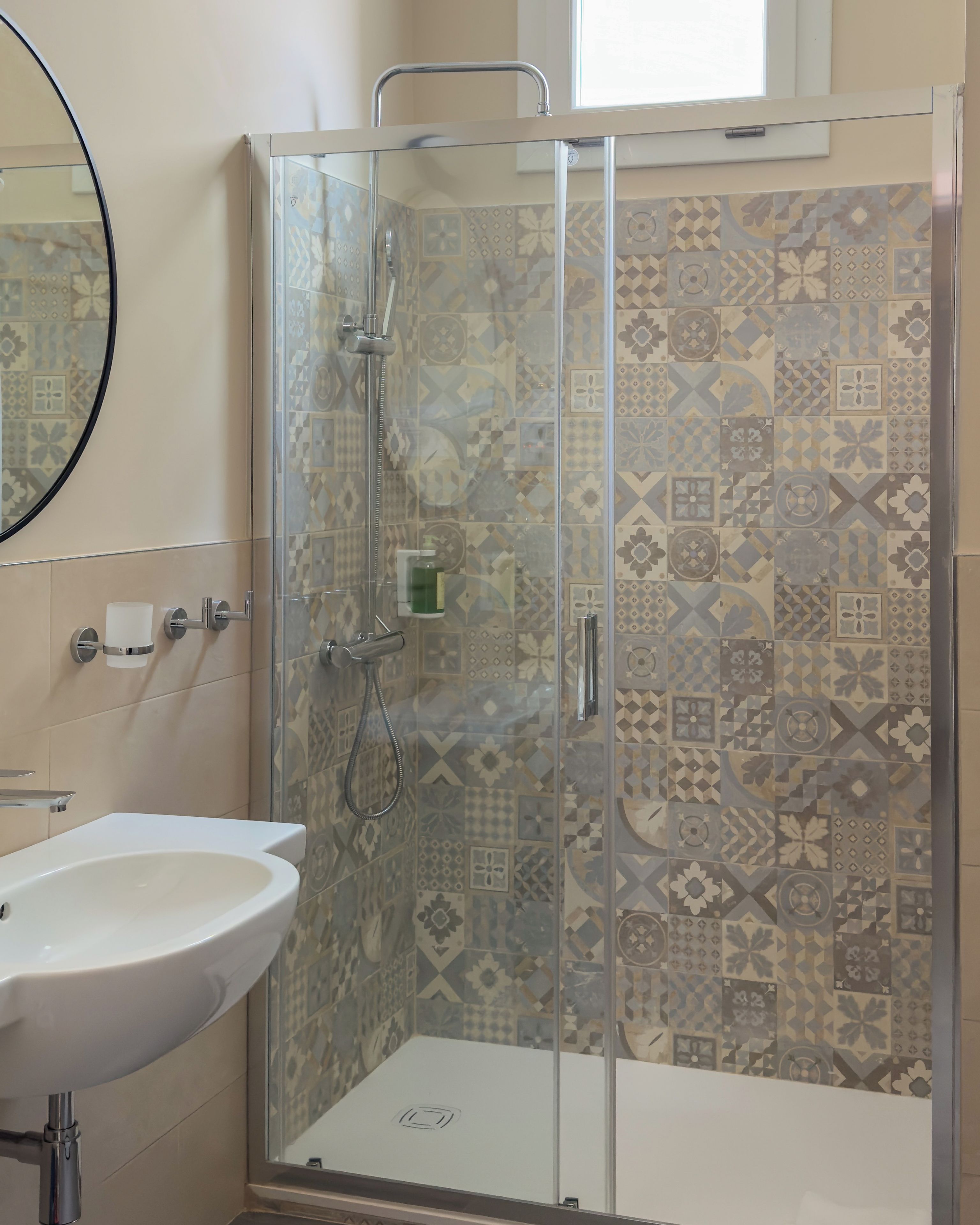 Une salle de bain avec une douche à parois de verre, un lavabo blanc et des carreaux à motifs.