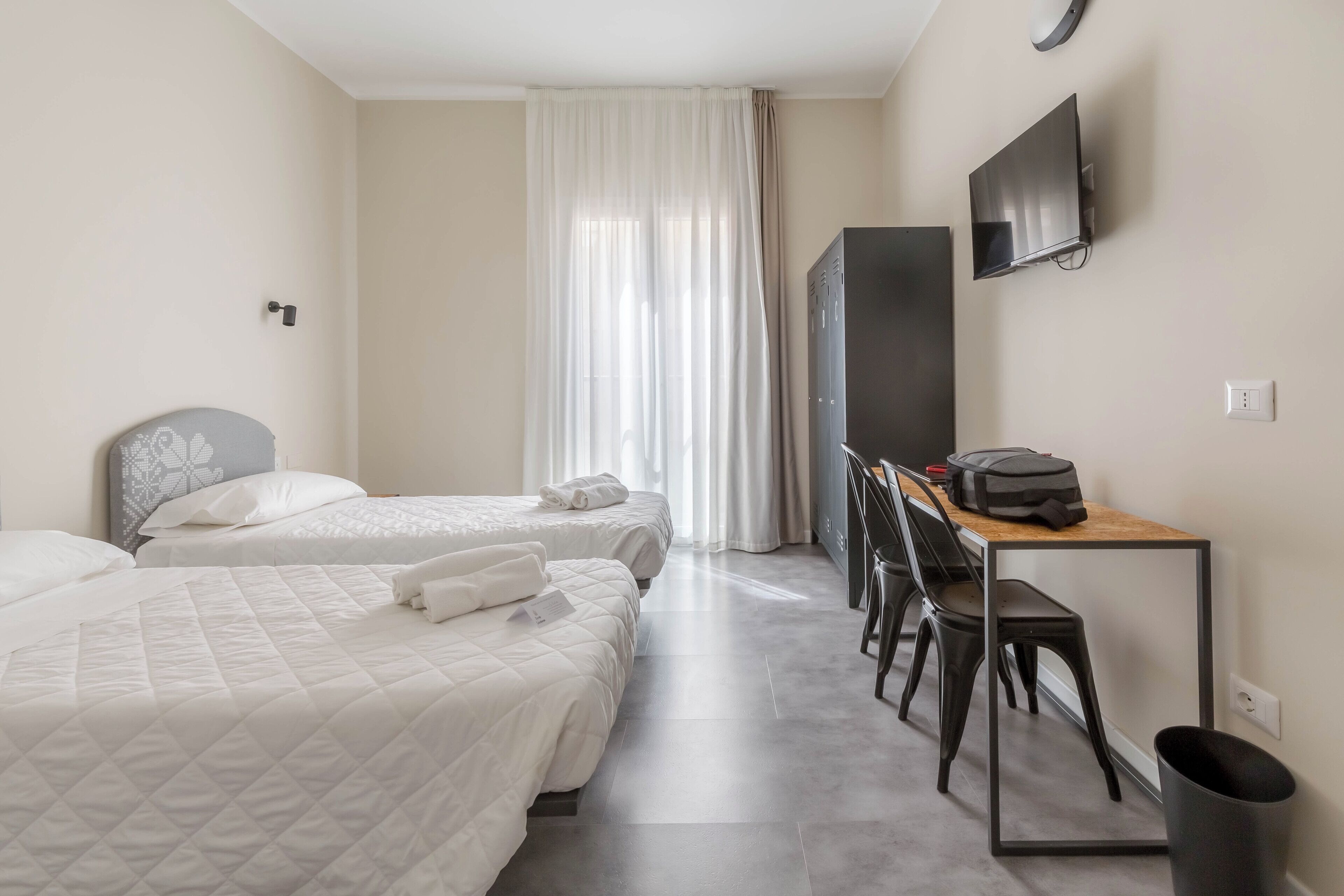 A hotel room with two beds, a desk with a chair, a television, and a wardrobe.