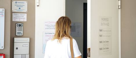 A person entering a hostel with a sign reading 'Piccolo Catalunya Hostel' and a door labeled 'INGRESSO ENTRANCE'.