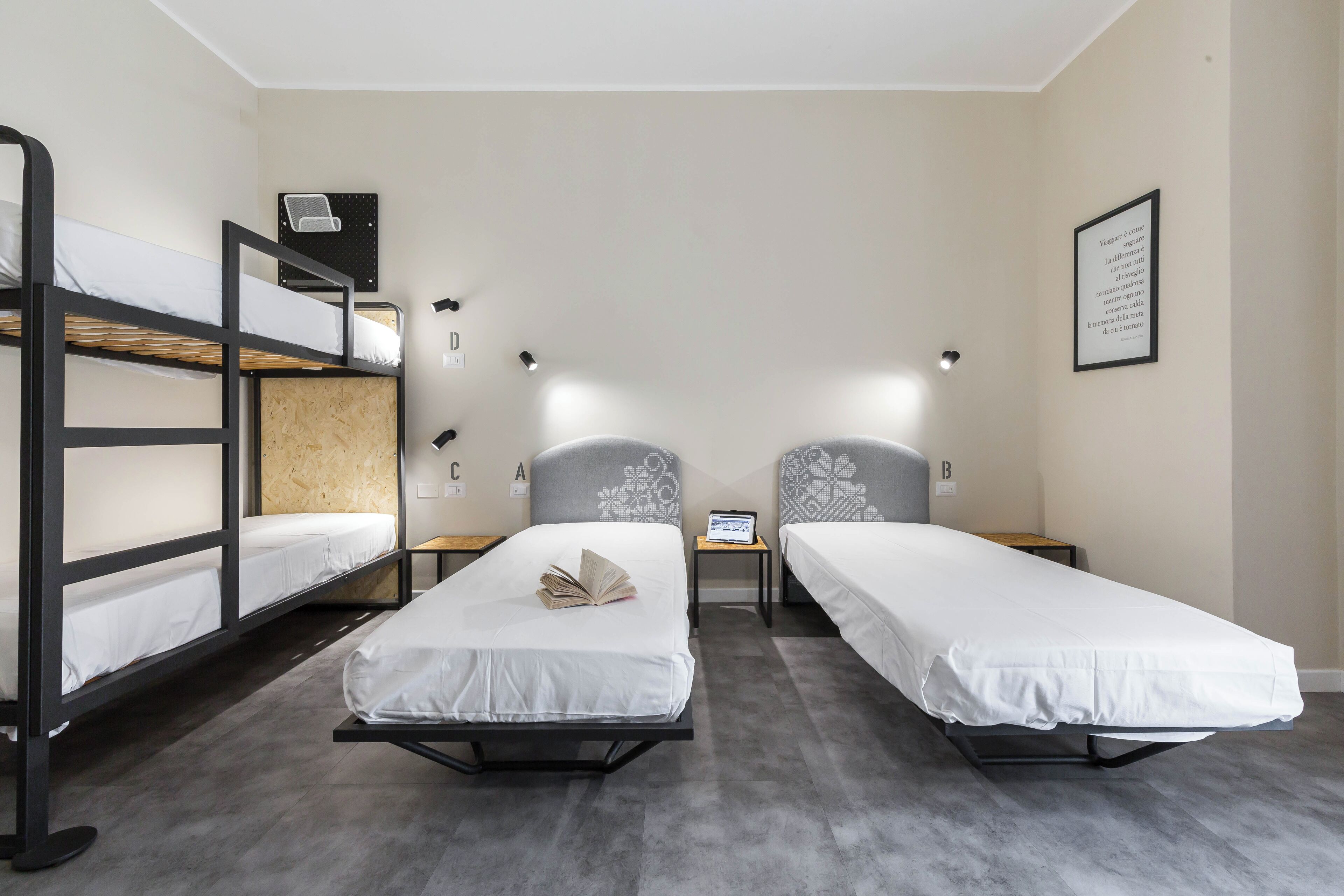 A room with two single beds, a bunk bed, a small table with a laptop, and a framed quote on the wall.