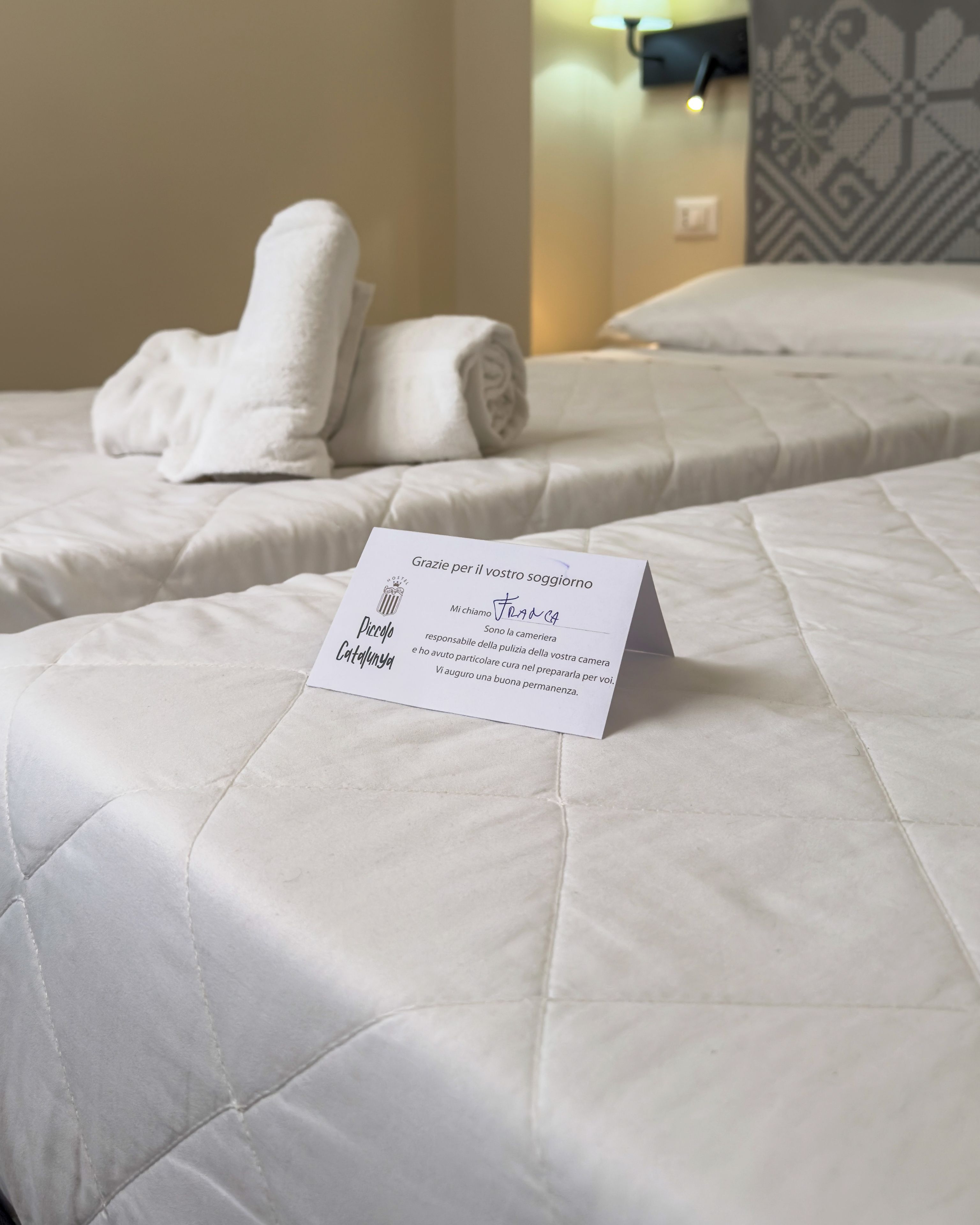 Une chambre d’hôtel avec deux lits, une serviette soigneusement pliée sur chaque lit et une carte de bienvenue posée sur le lit.