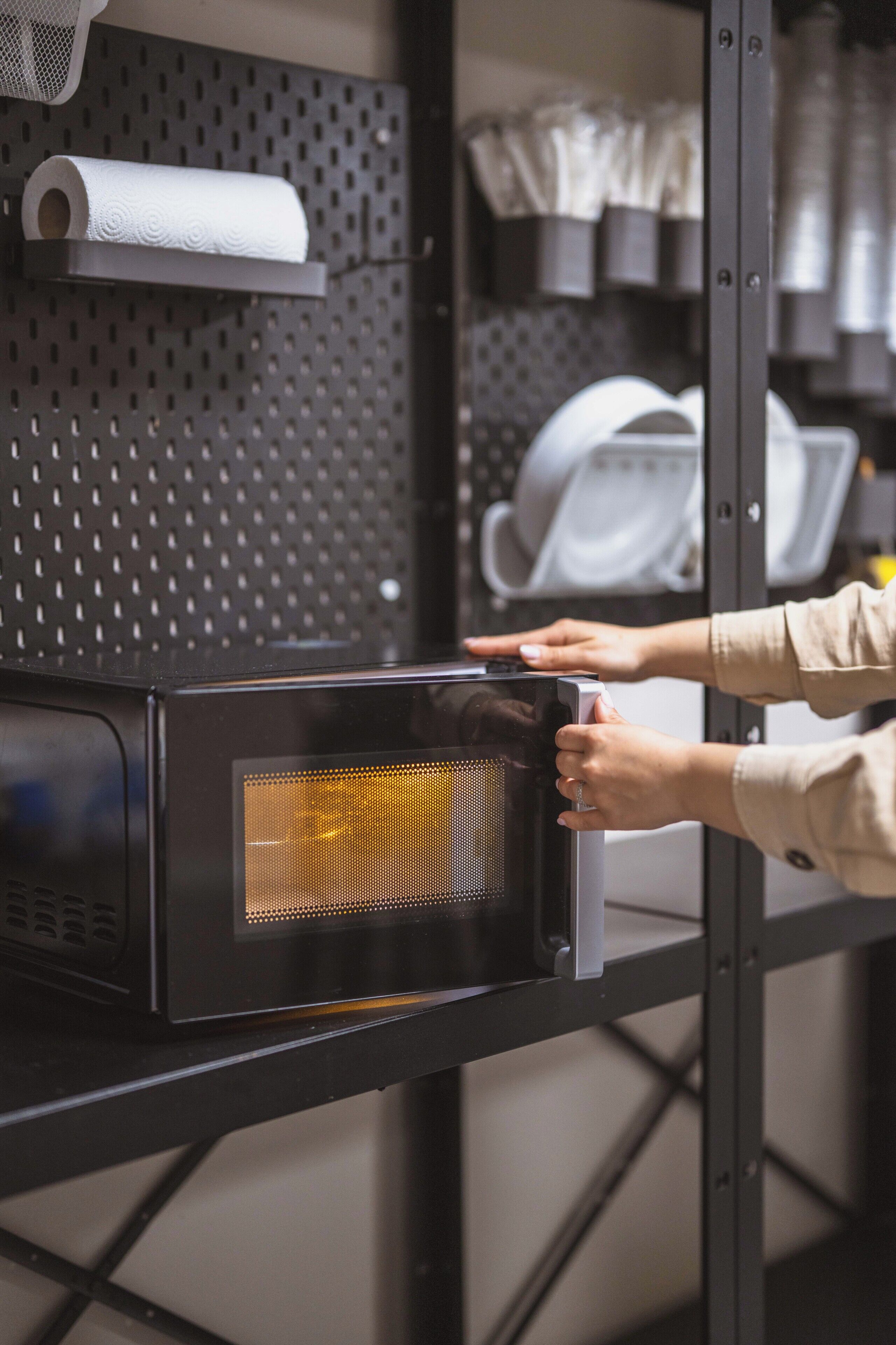 Un horno microondas sobre un estante con un panel metálico perforado al fondo.