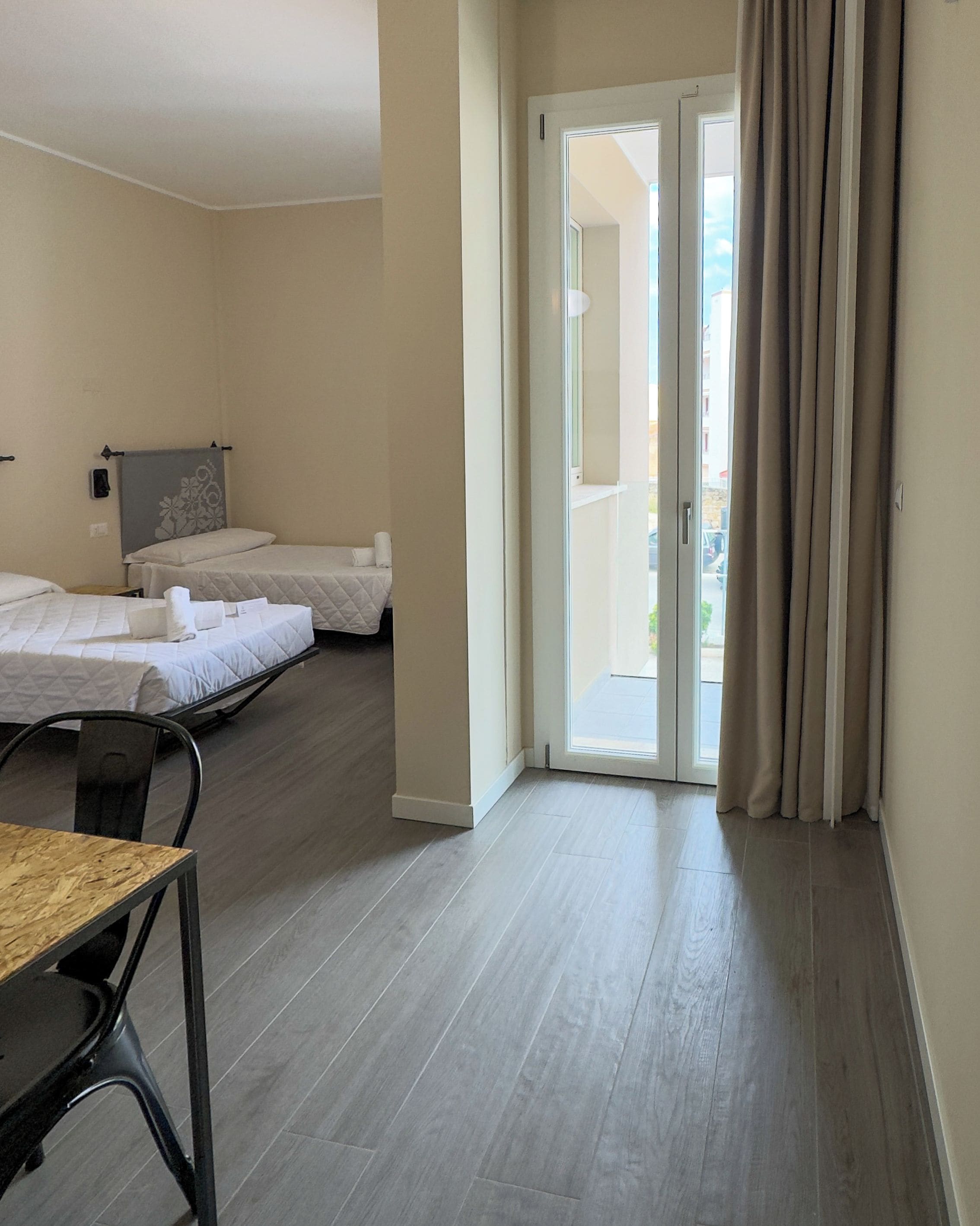 Habitación de hotel con dos camas, una mesa de comedor y un ventanal corredero que da a un espacio exterior.