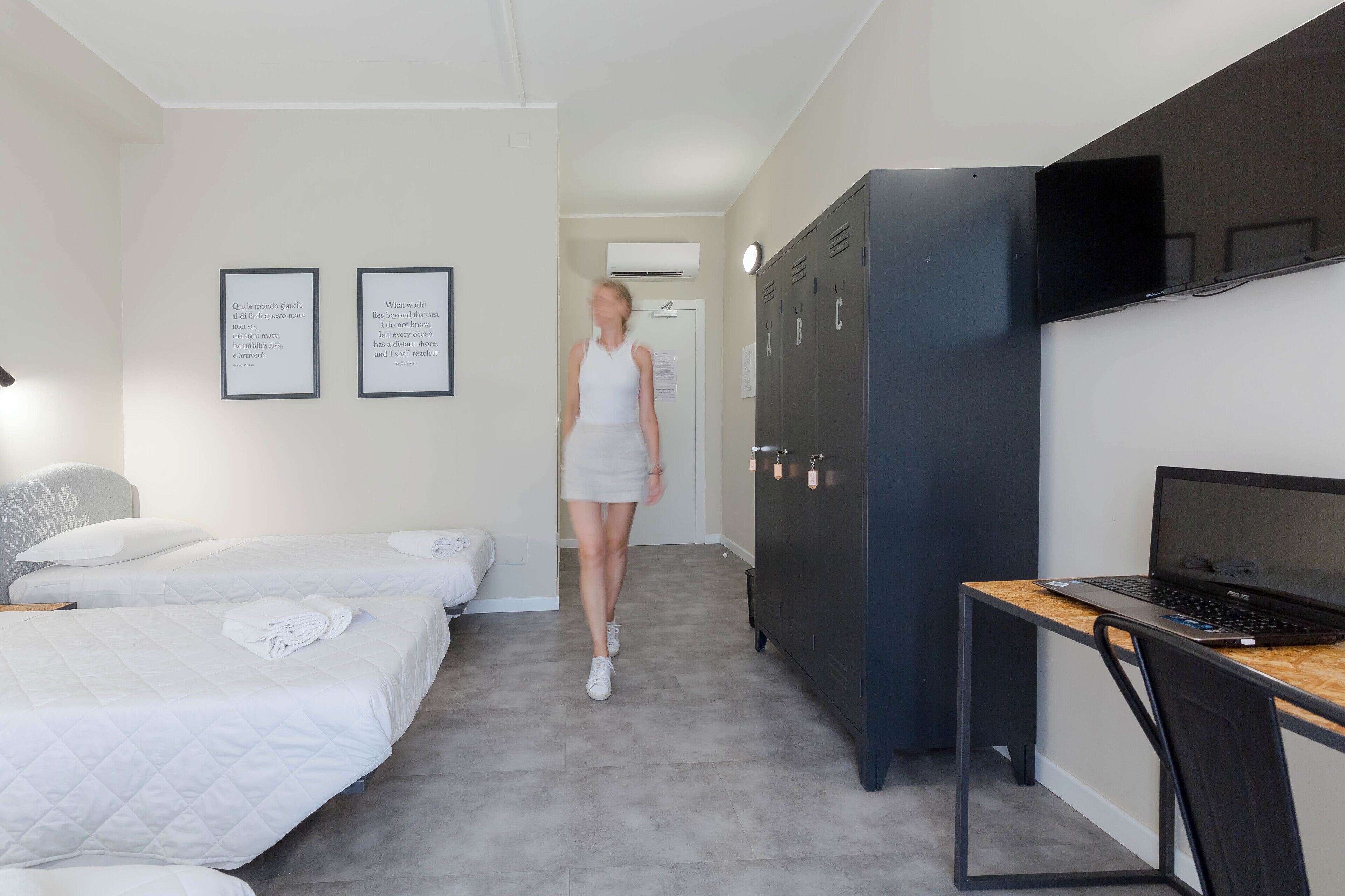 Een hotelkamer met twee bedden, een bureau met een laptop en een kledingkast.
