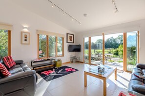 A spacious living room with a sofa, a coffee table, and a TV. Large windows offer a view of the outdoors. - 2 Bed in Stelling Minnis (oc-ek715) (Lyminge)