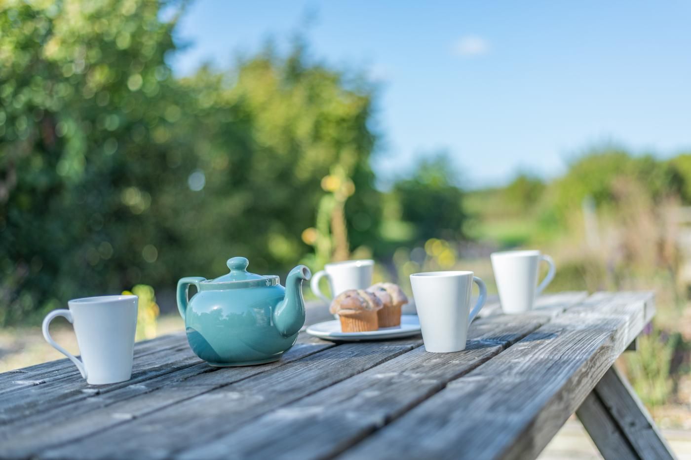 Ein Holztisch mit einem blauen Teekessel, weißen Tassen und Muffins.