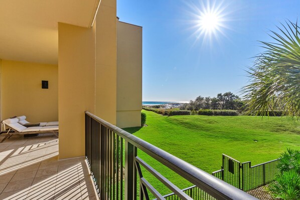 A balcony with a sun lounger and a view of a green lawn and distant landscape. - Amazing Condo on the Beach on 30A! (Santa Rosa Beach)