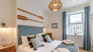 A neatly arranged hotel room with a large bed, a bedside table with a lamp, a window with curtains, and a city view. - 2 Bed in Amble (oc-l32947) (Amble)