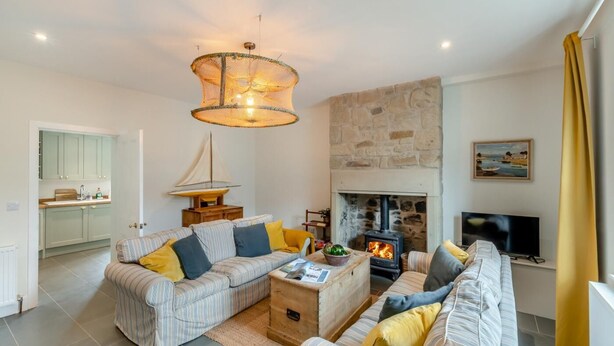 A cozy living room with a fireplace, striped sofas, and a sailboat model. - 2 Bed in Amble (oc-l32947) (Amble)