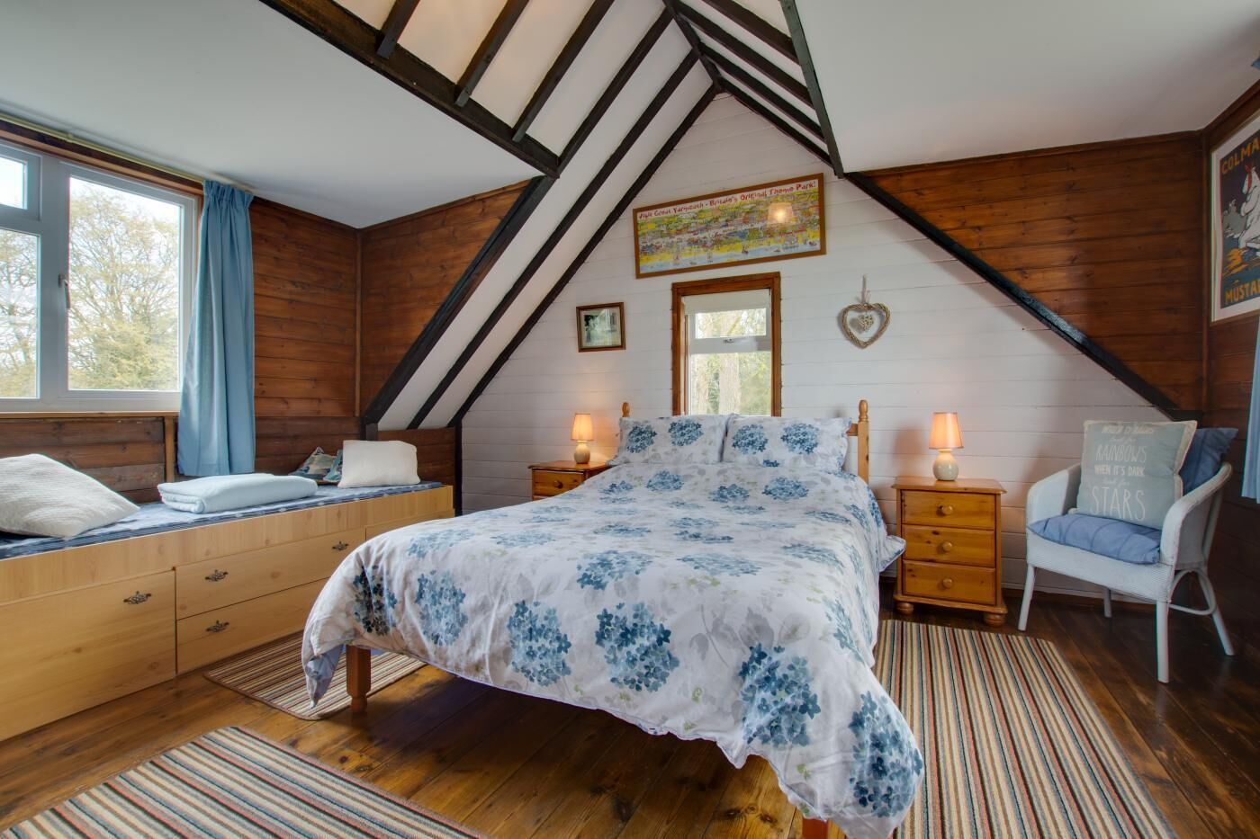 Un dormitorio con techo inclinado, cama con ropa de cama floral, muebles de madera y ventana con cortinas.