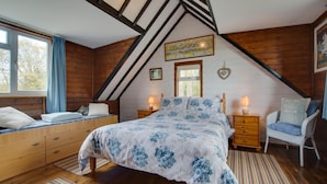 A bedroom with a sloped ceiling, a bed with floral bedding, wooden furniture, and a window with curtains. - 1 Bed in Southrepps (oc-1305) (Southrepps)