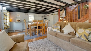 A cozy living room with a wooden staircase, a dining area with a table and chairs, and a kitchen with white cabinets. - 1 Bed in Southrepps (oc-1305) (Southrepps)