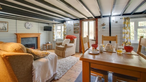 A cozy room with a fireplace, a television, a dining table set for breakfast, and a comfortable seating area. - 1 Bed in Southrepps (oc-1305) (Southrepps)