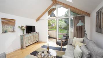 A spacious living room with a high ceiling, a television, a wooden cabinet, a sofa, and a coffee table with wine glasses.