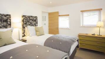 A bedroom with two beds, a wooden door, a dresser, and a window with blinds.