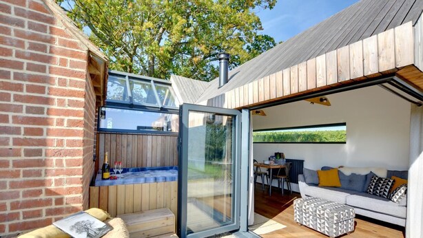 A modern outdoor living space with a glass door leading to a patio area, a wooden deck, and a cozy seating area with cushions and a patterned ottoman. - 1 Bed in Stone (oc-tn618) (Stone in Oxney)