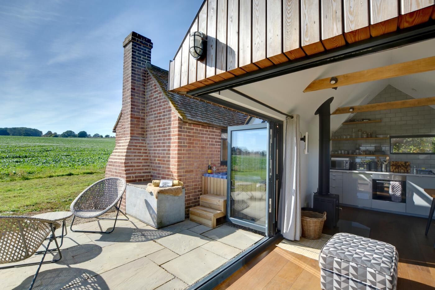 Un patio con chimenea de ladrillo, mobiliario exterior y vistas a un campo verde.