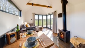 A modern living room with a fireplace, a dining table set with wine glasses and a bottle, and a sofa with a view of the outdoors. - 1 Bed in Stone (oc-tn618) (Stone in Oxney)