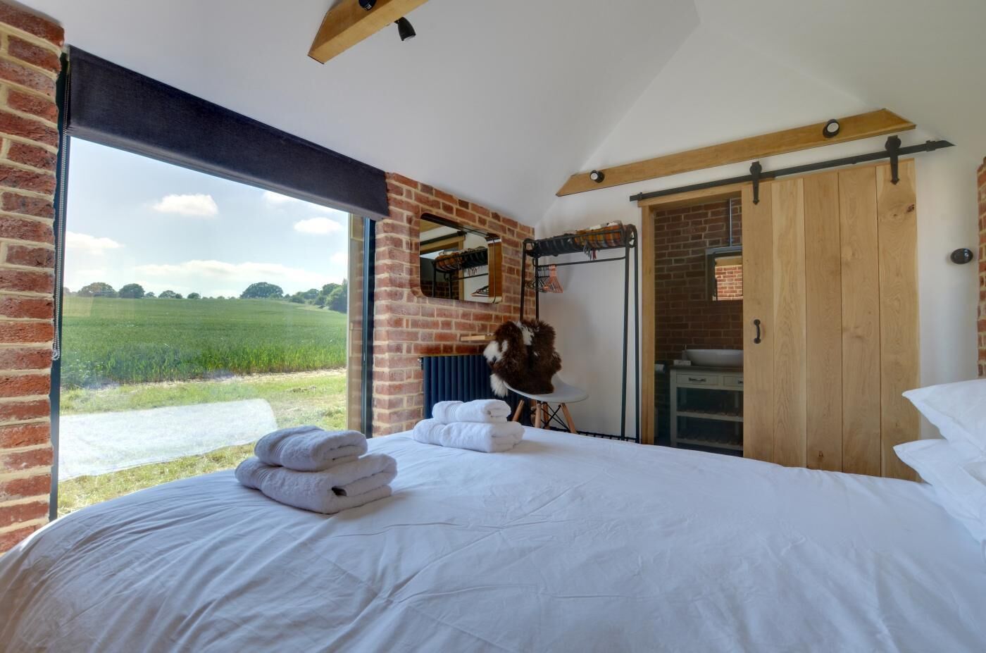 A bedroom with a large bed, a view of a field, a wooden door, and a brick wall.