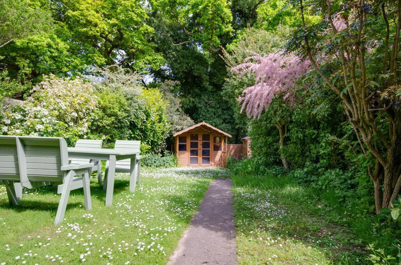 Un jardín con una cabaña de madera, una banca y un sendero.