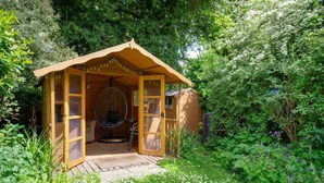 Una cabaña de madera con una silla mecedora, una mesita y una puerta de cristal.