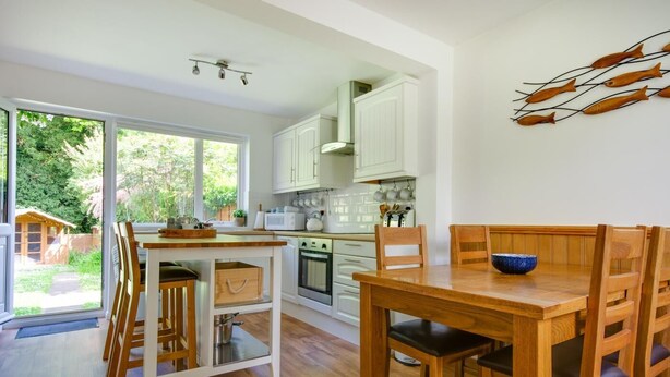 Una cocina moderna con armarios blancos, una mesa de comedor de madera y vistas al jardín.