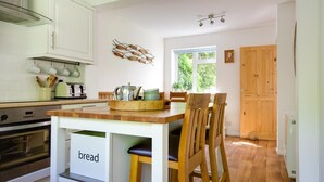 Una cocina moderna con armarios blancos, una mesa de comedor de madera y un mueble para pan.