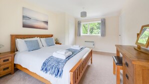 Un dormitorio con cama de madera, una mesita de noche, un escritorio con silla, una ventana con cortinas y un cuadro en la pared.