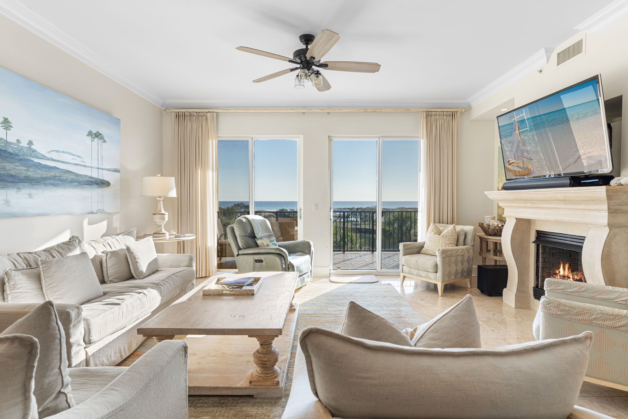A spacious living room with a large sofa, a coffee table, and a fireplace. There is a television mounted on the wall and a ceiling fan.