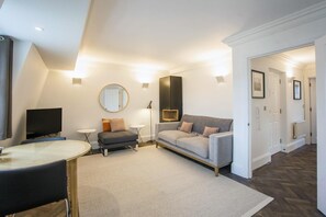 A modern living room with a sofa, a round mirror, a television, and a dining area. - 2 Bed in Bath (oc-bhr28) (Bath)