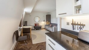 Un espace de vie compact comprenant un coin cuisine, un coin repas et un espace détente avec un canapé et un miroir rond.