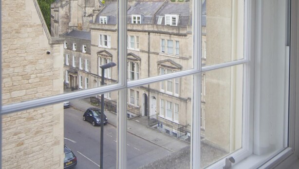 Une vue depuis une fenêtre donnant sur une rue bordée de bâtiments traditionnels, avec une voiture garée et un lampadaire.