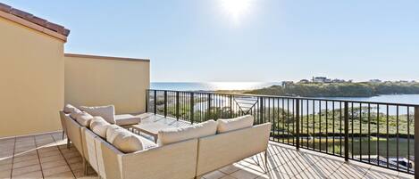 A balcony with a sofa and table, overlooking a body of water and greenery.