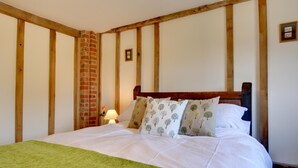 Un dormitorio con una cama grande, vigas de madera, una pared de ladrillo y una manta verde.