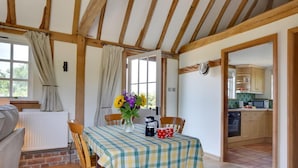 Un rincón comedor acogedor con una mesa lista para dos personas, un jarrón de flores y vistas a la cocina a través de un vano abierto.