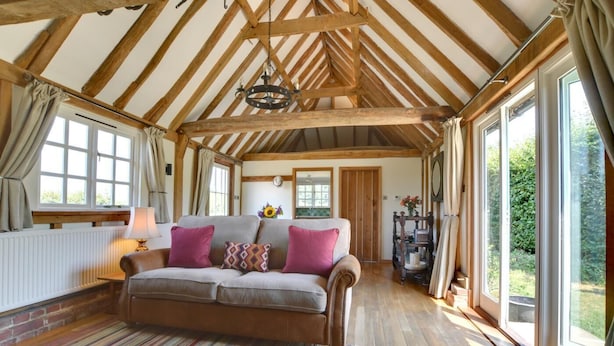 Una habitación acogedora con techo de madera, un sofá con cojines, un radiador y ventanas amplias.