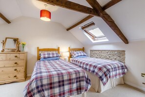 Een slaapkamer met twee bedden, een houten dressoir, een dakraam en een stenen muur.