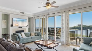 A spacious living room with a large window, a ceiling fan, and a view of the sea. - Family Friendly Beachfront Escape (Santa Rosa Beach)