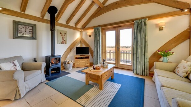 A cozy living room with a fireplace, sofas, a television, and a view through a large window. - 2 Bed in Tenterden (oc-tn606) (Stone in Oxney)