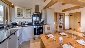 A modern kitchen with granite countertops, white cabinetry, and a dining area with a wooden table and chairs. - 2 Bed in Tenterden (oc-tn606) (Stone in Oxney)