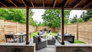 Patio esterno con pergolato in legno, mobili in vimini e un piccolo prato.